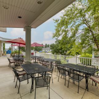 An inviting outdoor patio area with tables and chairs, shaded by umbrellas and surrounded by lush trees.