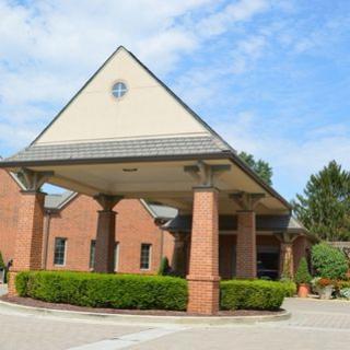 A brick building with a covered entrance and surrounding greenery under a clear sky.