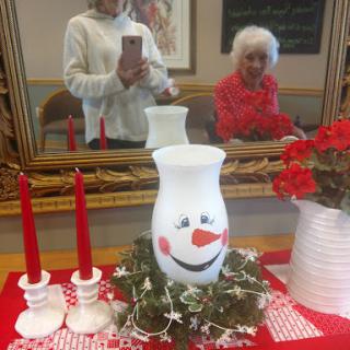 A cheerful holiday decoration featuring a smiling vase centerpiece, red candles, and lovely flowers.