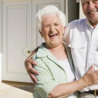 An elderly couple smiling warmly while standing outdoors.