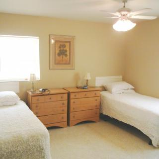 A cozy bedroom with two single beds, a dresser, and a ceiling fan.
