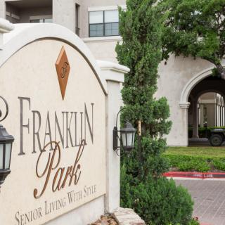 Entrance sign for Franklin Park with surrounding greenery and a view of the building in the background.