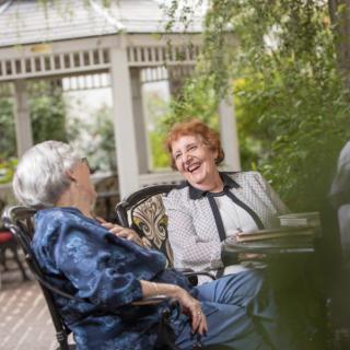 Two elderly women enjoying a conversation in a garden setting.