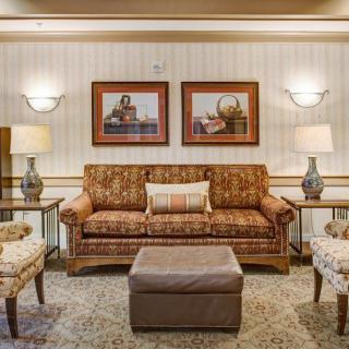 A cozy living room with a patterned sofa, two armchairs, and a central ottoman, elegantly decorated with lamps and artwork on the wall.