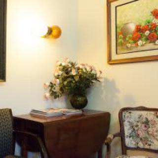 A cozy room with a corner table adorned with flowers, adjacent to ornate chairs and a vibrant painting on the wall.