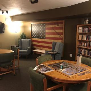 A cozy reading room featuring a large American flag on the wall, bookshelves, and comfortable seating areas.