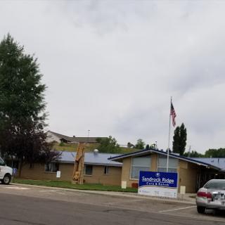 A community building under a cloudy sky, featuring a flag and visible vehicles in the foreground.