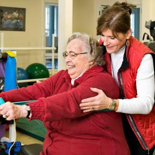 An elderly woman engaging in physical therapy with the assistance of a caregiver.