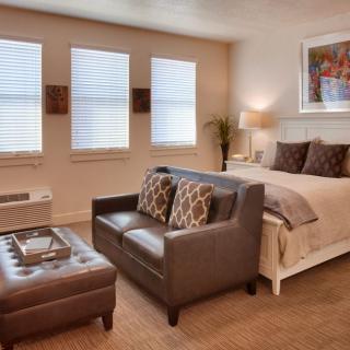 A cozy bedroom with a small living area, featuring a leather sofa and a neatly made bed in modern neutral tones.