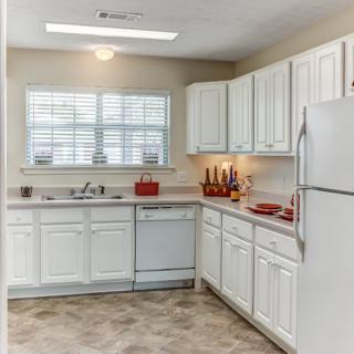 A modern kitchen with white cabinets, featuring a refrigerator, dishwasher, and spacious countertop.