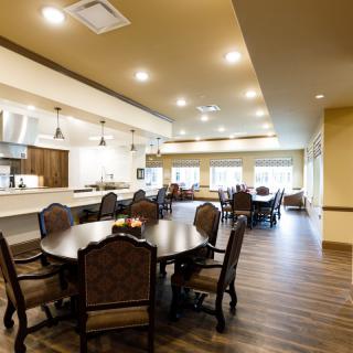A spacious and well-lit dining area with round wooden tables and upholstered chairs.