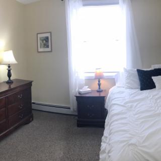 A cozy bedroom with a bed, dresser, and lamps by the window.