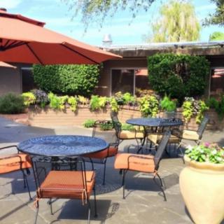 A cozy patio with tables and chairs under a large umbrella surrounded by lush greenery.