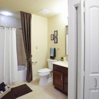 A modern bathroom with beige walls, featuring a shower curtain, toilet, sink with vanity, and mirror.