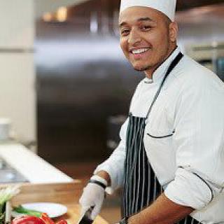 A chef in a kitchen preparing to cook, smiling at the camera.