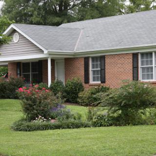 A charming single-story brick house with a well-maintained front yard and colorful landscaping.
