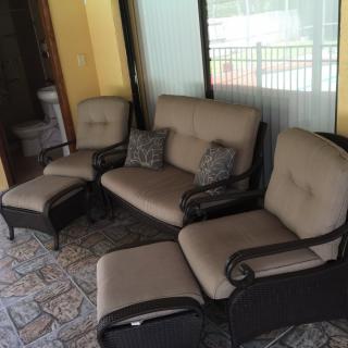 A cozy outdoor seating area featuring a sofa and chairs with cushions on a tiled patio.