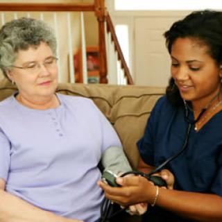 A nurse measures blood pressure for an elderly woman during a home visit.