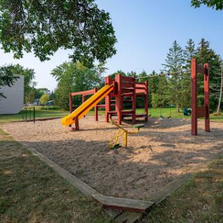 A colorful playground with a slide set in a sandy area surrounded by trees.