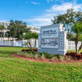 A view of the Grand Villa senior living community with well-maintained landscaping and clear signage.