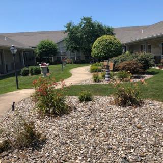 A well-maintained courtyard featuring a pathway, bushes, and trees under a clear blue sky.