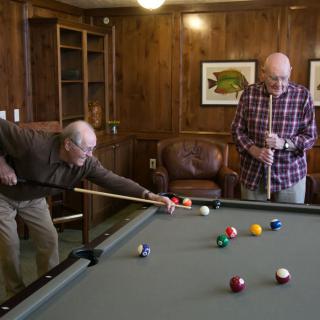 Two seniors enjoy a game of billiards in a cozy room.