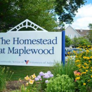 Entrance sign for The Homestead at Maplewood surrounded by colorful flowers and lush greenery.
