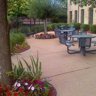 A peaceful outdoor patio area with tables and chairs surrounded by lush greenery and flowers.