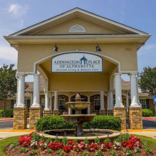 An entrance to a building with a sign and landscaped flower bed.