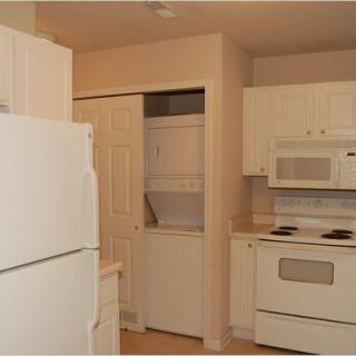 A cozy kitchen featuring white cabinets and appliances, including a stove, microwave, refrigerator, and a laundry closet.