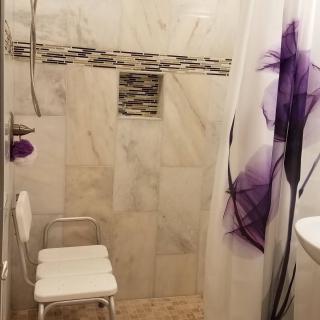 A bathroom shower area with a marble tiled wall and a chair, featuring a decorative purple shower curtain.