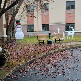 A festive winter scene featuring a snowman and reindeer decorations set in a park-like area with fallen leaves.