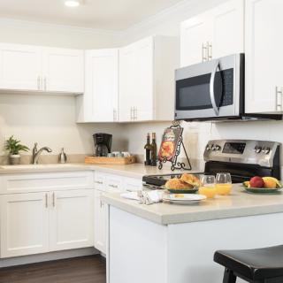 A modern kitchen with white cabinets, equipped with appliances and fruit on the countertop.