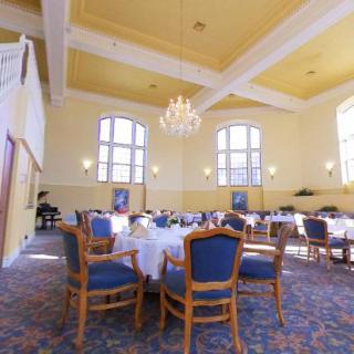A spacious dining room with elegantly set tables, chairs, large windows, and a chandelier.