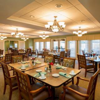 A well-lit dining area with neatly arranged tables and chairs, illuminated by chandeliers.