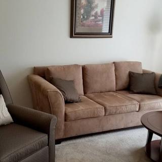 A cozy living room featuring a beige sofa with cushions, an armchair, and a wooden coffee table beneath a decorative painting.