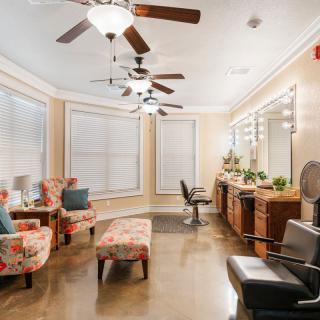 A well-lit salon interior with comfortable seating, multiple mirrors, and ceiling fans.