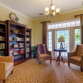 A cozy library room with bookshelves, armchairs, and large windows.
