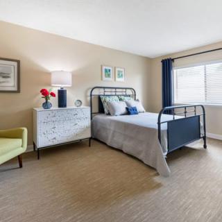 A cozy and well-decorated bedroom featuring a metal bed frame, a dresser with decorative items, and a comfortable chair by the window.