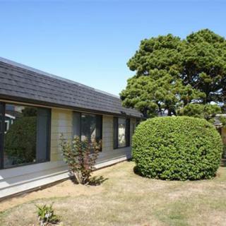 A suburban house with large windows, surrounded by a well-maintained lawn and neatly trimmed bushes on a sunny day.