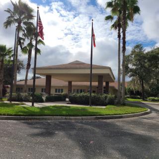 A welcoming entrance of a commercial building surrounded by palm trees and flags under a partly cloudy sky.