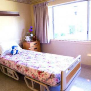 A bright room with a hospital bed, floral bedspread, and large window.