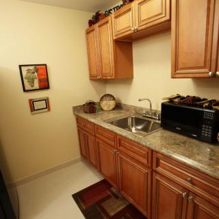 A compact kitchen with wooden cabinets, a countertop sink, and a microwave.