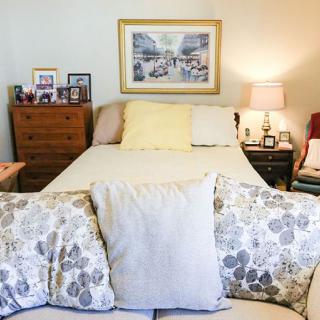 A cozy bedroom setup with a neatly made bed, decorative pillows, bedside tables, lamps, and framed artwork on the wall.