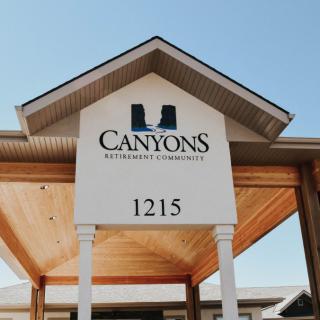 The entrance sign of Canyons Retirement Community displaying the address 1215 under a clear blue sky.