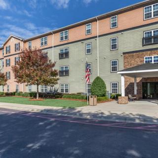 A multi-story residential apartment building with a front entrance and surrounding trees.