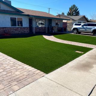 A well-maintained lawn with artificial grass in front of a home, showcasing neat landscaping and a paved driveway.