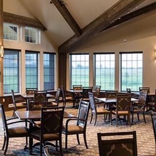 An empty dining room with tables and chairs, featuring large windows and a vaulted ceiling.