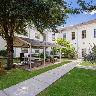 A peaceful garden area with a shaded patio and seating in front of a building.