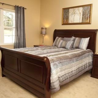 A cozy bedroom with a wooden sleigh bed, striped bedding, and wall art above.